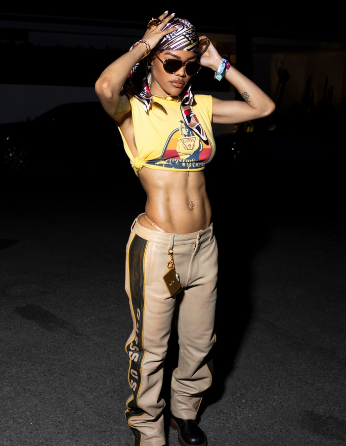 Teyana Taylor showing toned Coachella abs wearing sunglasses, a headscarf, and casual festival outfit at night.