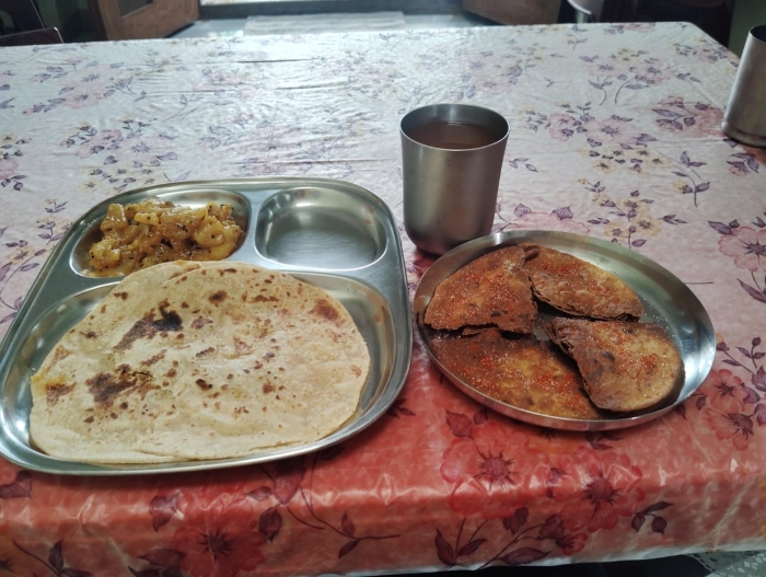Indian meal with flatbreads, potato curry, spiced parathas, and drink on a floral table. Suitable for transitioning into vegan.