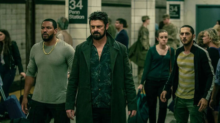 Three men walking in a crowded subway station scene from The Boys amid fans boycott over controversial army history. Three men walking in a crowded subway station scene from The Boys amid fans boycott over controversial army history.