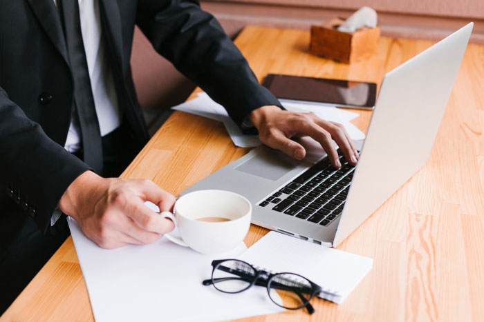 Man in suit using laptop and holding coffee cup at wooden desk, representing HOA demands and trampoline dispute.