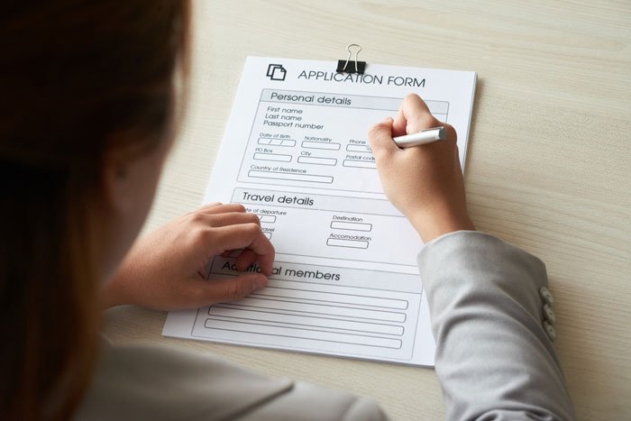 Person filling out an application form by hand at a desk, relating to HOA demands and community board decisions.
