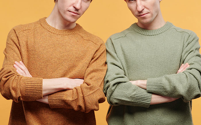 Two identical twins standing with arms crossed against a yellow background in a paternity update case.