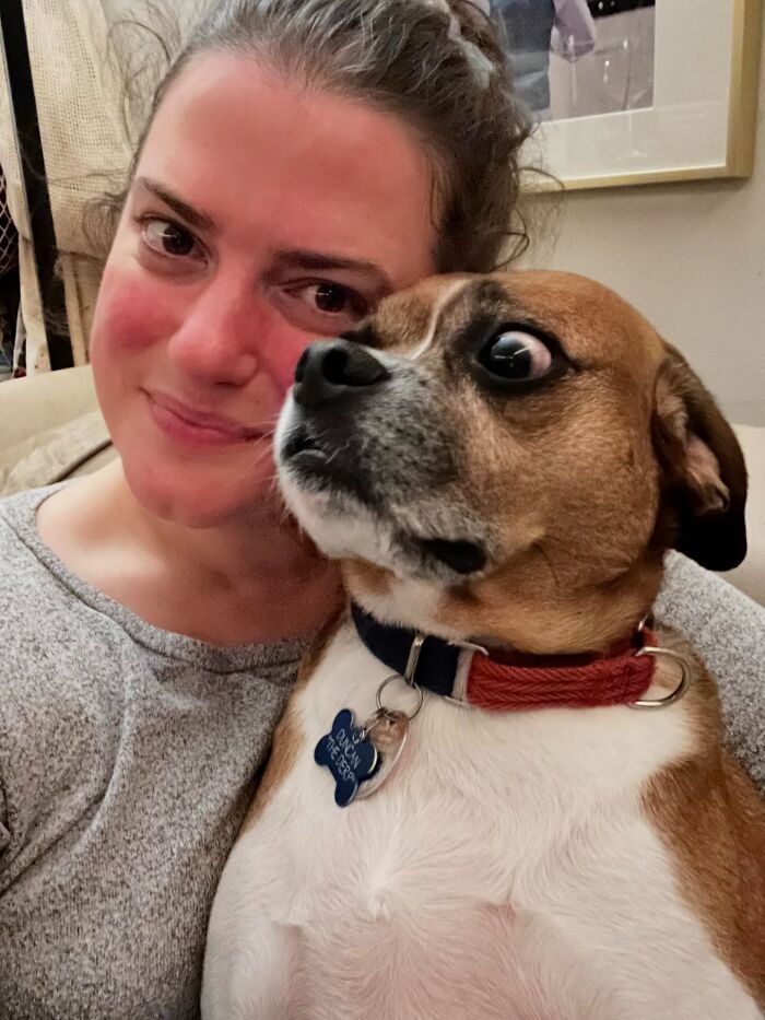Woman smiling with an unhinged pet dog looking wide-eyed and anxious, capturing adorable unhinged pet chaos moments.