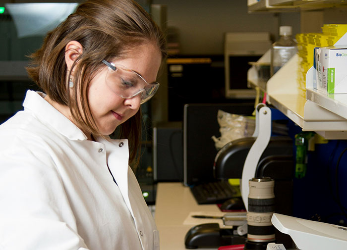 Young woman in a lab coat and safety glasses working creatively in a laboratory setting for job success.