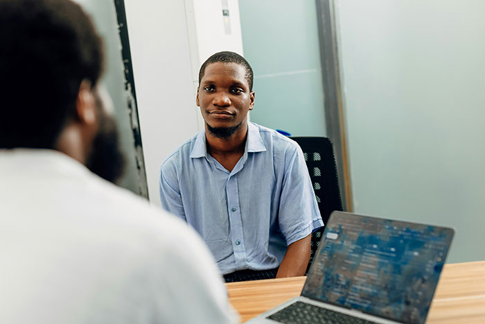 Man in a blue shirt creatively interviewing for a job across from a person with a laptop in an office setting.
