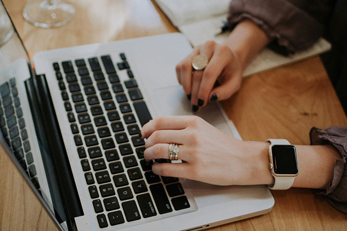 Hands with rings and smartwatch typing on a laptop keyboard, illustrating creativity in ways to successfully get a job.