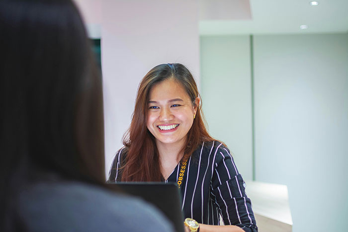 Young woman smiling confidently during a job interview, showcasing creative and sneaky ways to successfully get a job.