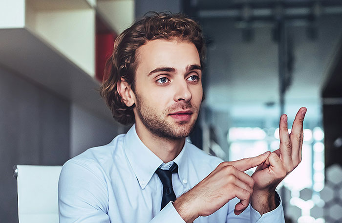 Young man in a light blue shirt explaining a creative and sneaky approach to successfully get a job in an office setting.
