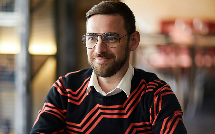 Man wearing glasses and a black and red sweater smiling thoughtfully representing creative ways to get a job successfully