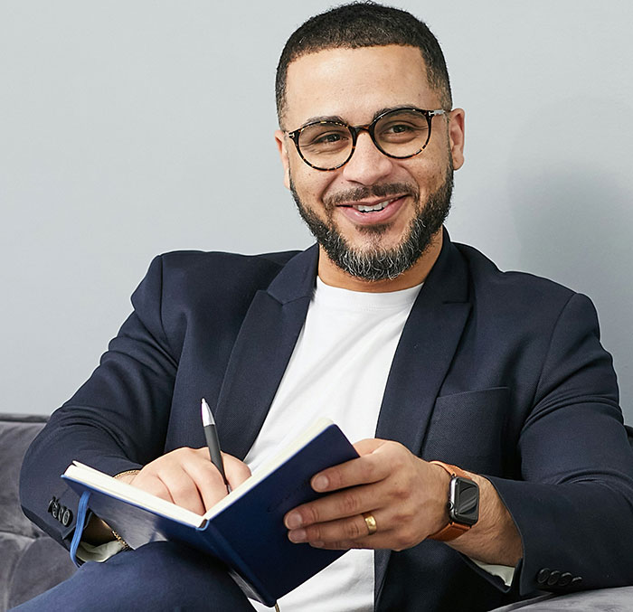 Man in glasses and blazer smiling while writing in a notebook, showcasing creative and sneaky ways to get a job.