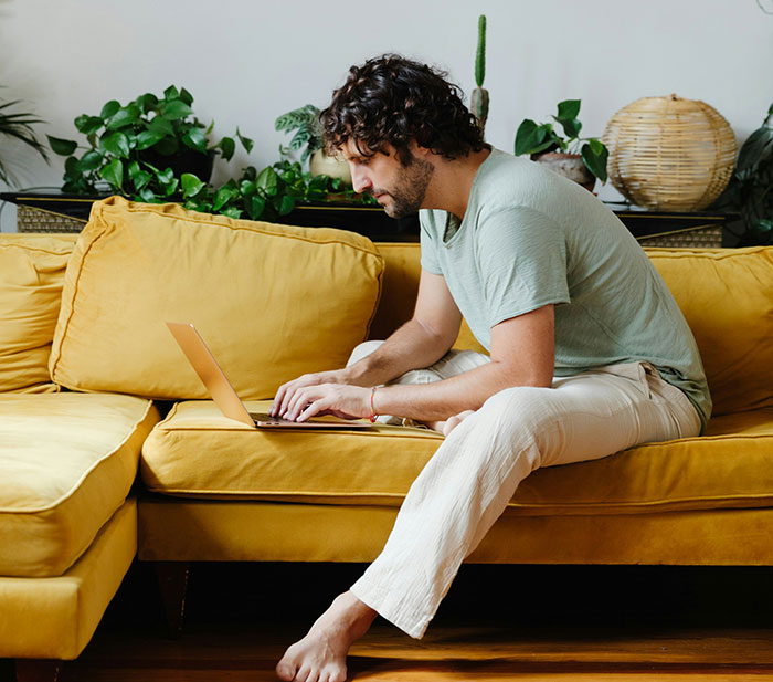 Man sitting on yellow couch working on laptop, demonstrating creativity and sneakiness to successfully get a job.