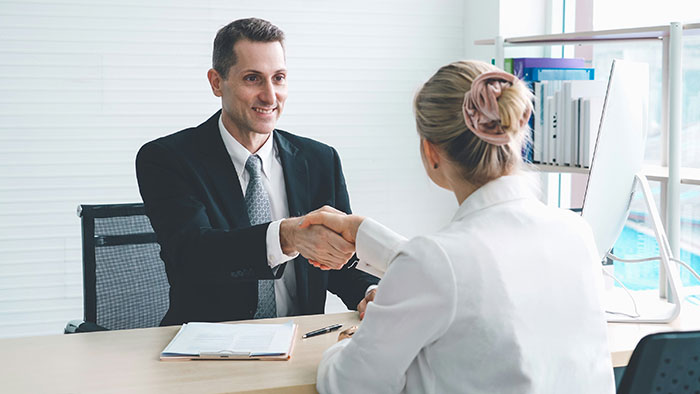 Man in a suit shaking hands with woman in an office during a creative and sneaky job interview to successfully get a job