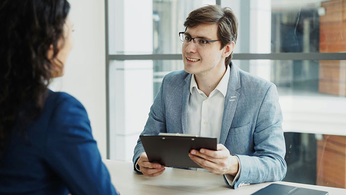 Man in a gray blazer conducting a job interview with a woman, demonstrating creative and sneaky job strategies.