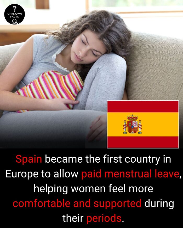 A woman on a couch with a hot water bottle, next to the Spanish flag, sharing interesting facts about paid menstrual leave.