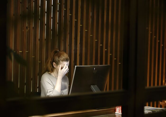 Woman at computer in office, appearing stressed or tired, highlighting jobs AI can’t touch in modern workplaces.