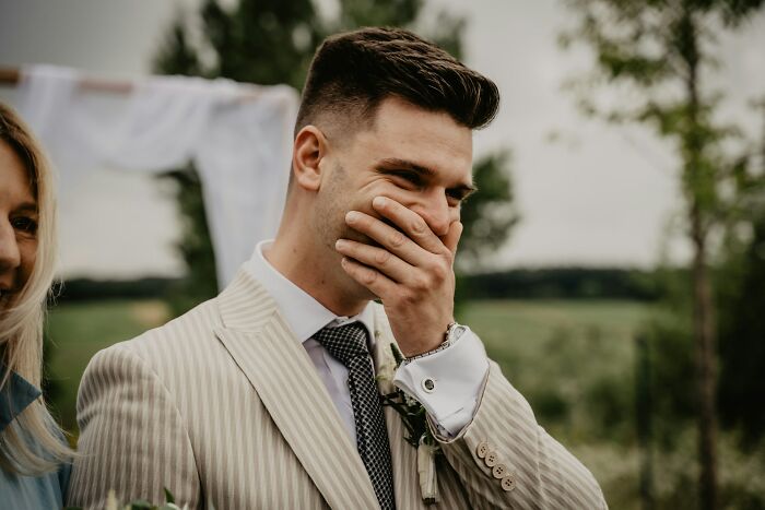 Groom at outdoor wedding, wearing striped suit and tie, showing emotion as guests witness a future breakup moment.