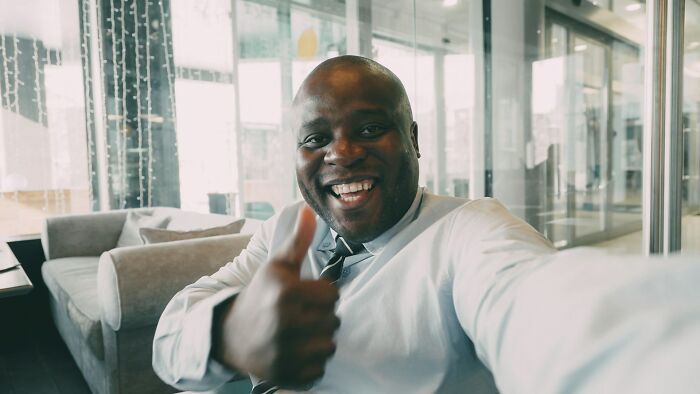 Smiling man giving thumbs up in a modern office, illustrating stories of random life decisions leading to the right place.