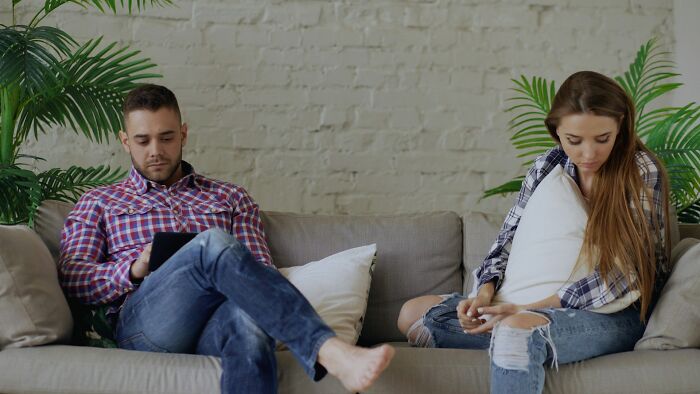 Couple sitting apart on a couch, avoiding eye contact, illustrating signs of a future breakup witnessed by wedding guests.