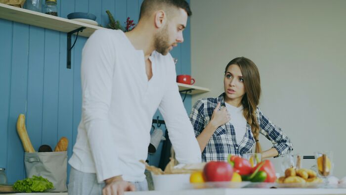 Man and woman having a tense conversation in kitchen illustrating weaponized incompetence in a domestic setting.