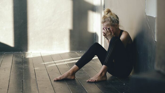 Woman sitting on wooden floor against wall with face in hands, illustrating dark family secrets and emotional distress.