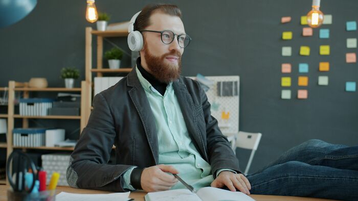 Man wearing headphones and glasses, sitting casually at desk with pen and open notebook, illustrating jobs AI can’t replace.