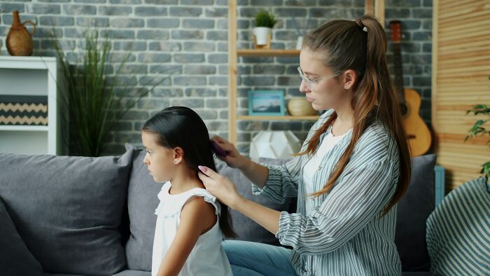 A young woman with glasses combs a little girl's dark hair. A scene portraying advice for dads raising daughters.