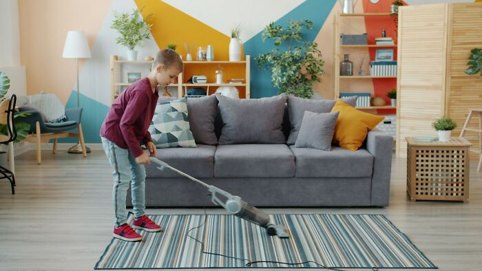 Young boy vacuuming carpet in living room, illustrating normal things people did with their families but now find bizarre.