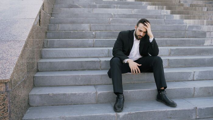 Man in a black suit sitting on outdoor stairs, looking stressed, reflecting on jobs AI can't replace.