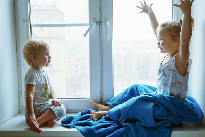 Two kids sitting on a windowsill playing, illustrating childhood moments with no survival instincts.