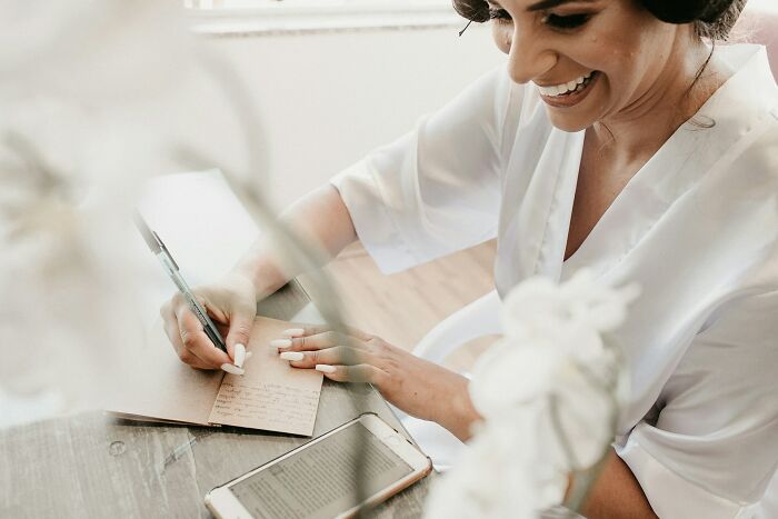 Smiling woman writing notes at a desk with a smartphone nearby, sharing parenting tips and tricks.