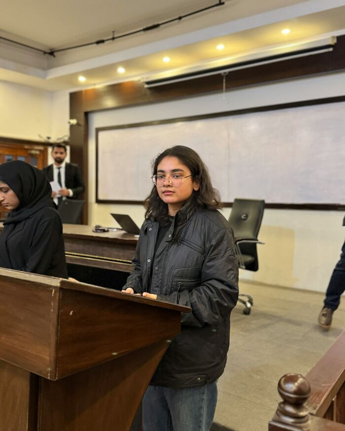 Young woman displaying intelligence confidently presenting in a classroom setting with others in the background.