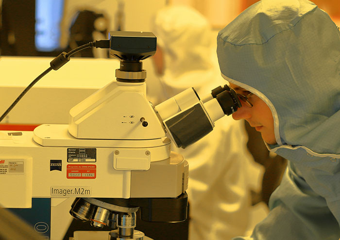 Scientist in protective gear examining samples under a high-tech microscope exploring unproven scientific theories.