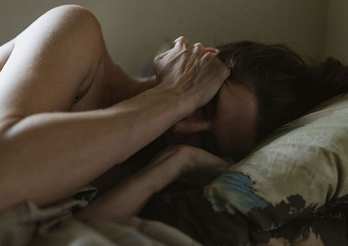 Person lying in bed with hand on forehead, reflecting on unproven scientific theories and ideas shared by experts.