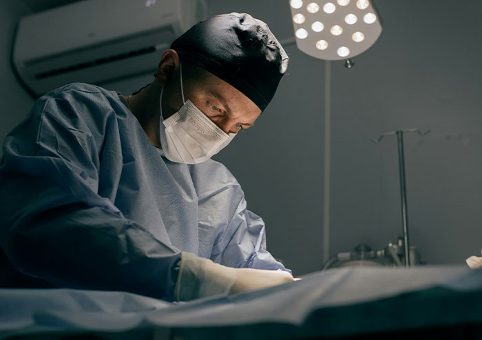 A scientist in surgical attire and mask focused on work under bright surgical lights, representing unproven scientific theories.
