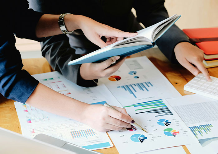 Two scientists analyzing charts and graphs on paper and in a book, discussing unproven scientific theories.