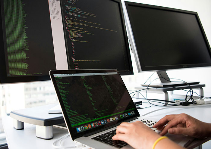 Person working on laptop and coding on multiple screens, illustrating scientists exploring unproven theories and data analysis.