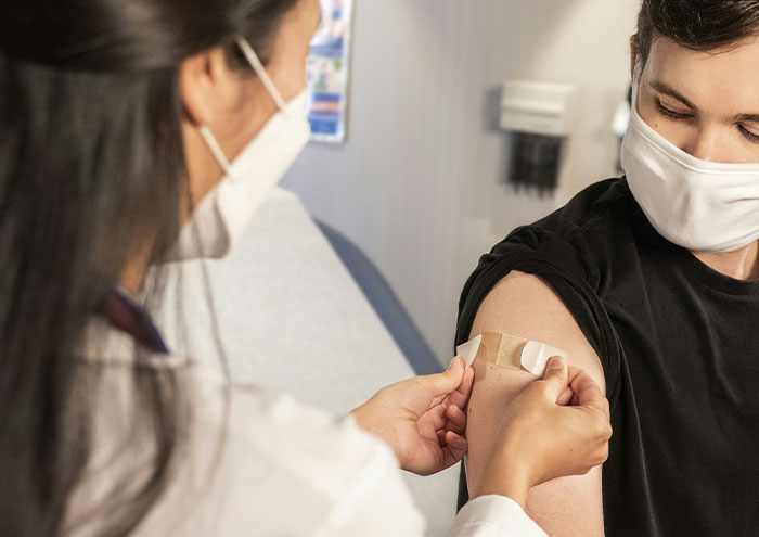 Scientist applying a bandage to a patient’s arm after vaccination, illustrating theories not yet proven in science.