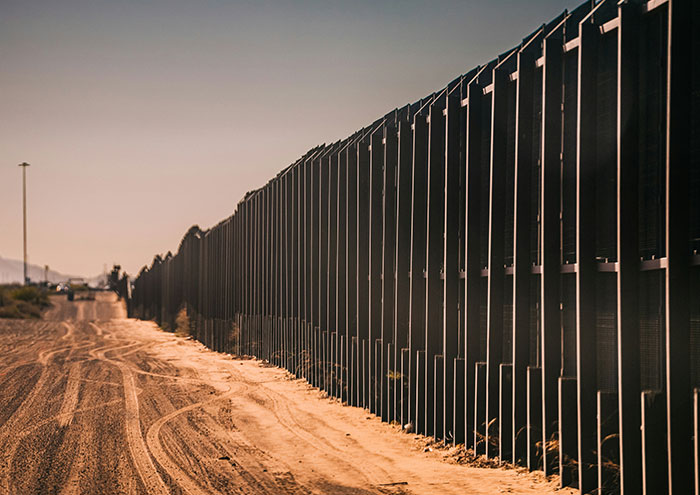 Border fence in desert landscape under clear sky illustrating major unproven theories shared by scientists.