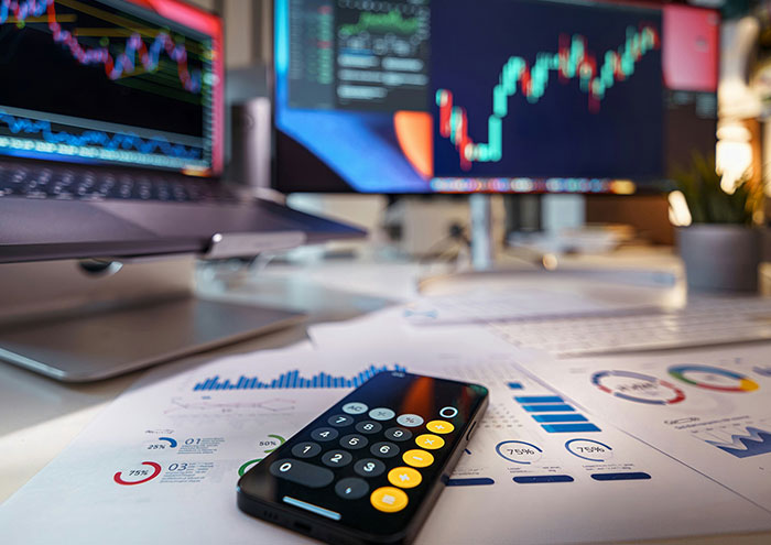 Calculator on printed charts and graphs in front of computer screens showing data, related to scientists' biggest theories.