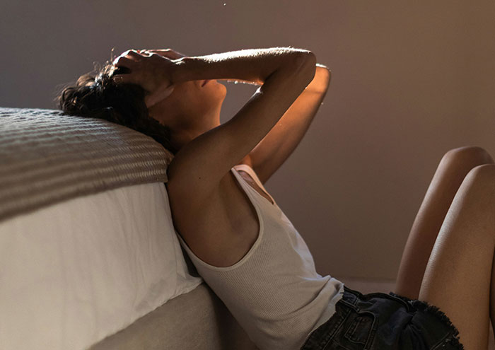 Person sitting on the floor leaning against a bed, reflecting on unproven scientific theories and concepts shared by scientists.