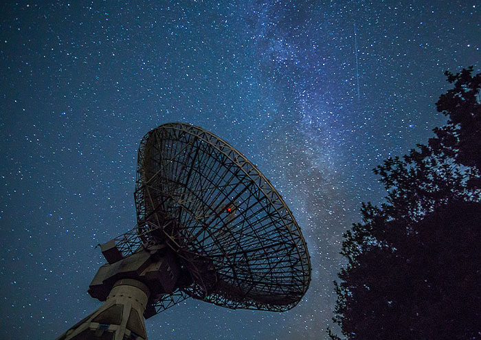 Large radio telescope dish pointed at starry night sky, symbolizing scientists exploring unproven scientific theories.