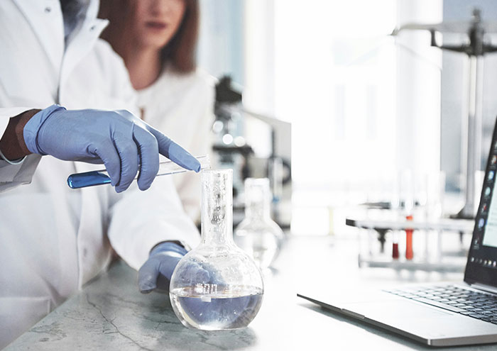 Scientist in lab coat conducting experiments with glassware and laptop, exploring unproven scientific theories.