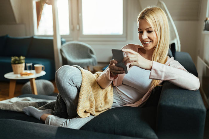 Woman relaxing on a couch using smartphone at home, illustrating a bedroom twist in a marriage story.