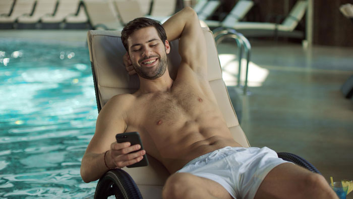 Smiling man relaxing on a poolside lounge chair, holding phone, enjoying leisure time after marriage twist.