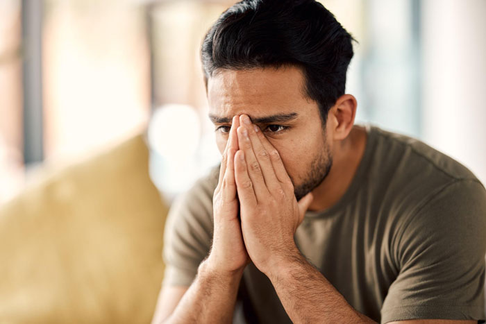 Man sitting indoors with hands covering mouth, appearing worried and emotional, related to cancer and divorce fear.