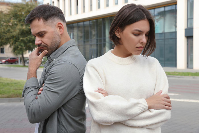 Woman and man standing back to back outdoors, both appearing upset and deep in thought, reflecting relationship fear and regret.