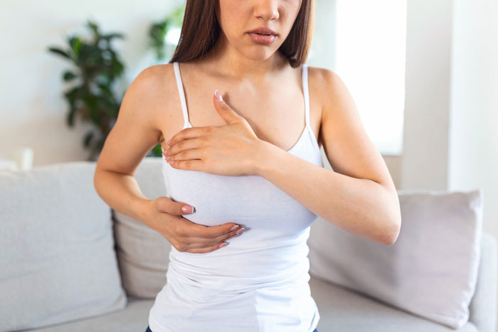 Woman in white tank top performing a breast self-exam related to cancer fear and relationship issues.