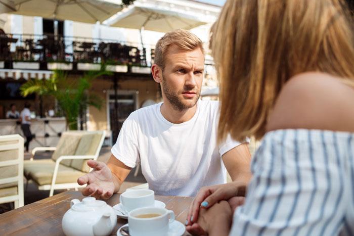 Couple having a serious conversation at an outdoor cafe, depicting fear of leaving during cancer and seeking a second chance.