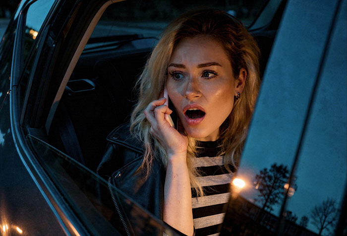 Woman in a car looking shocked while on phone, illustrating wife discovering evidence of husband&rsquo;s affair and revenge.