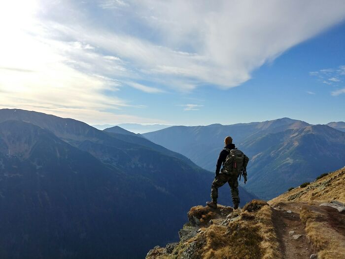 Hiker standing on a mountain cliff overlooking vast peaks, symbolizing unexpected and bizarre ways people passed away.